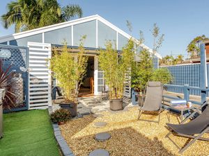 Exterior view of a small blue cottage with white trim, double glass doors, potted bamboo and outdoor seating.