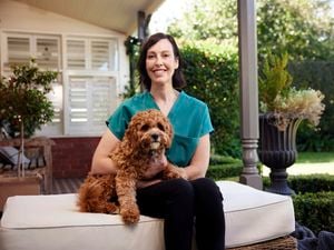 Handler and puppy sitting on a cushion in an outdoor area.