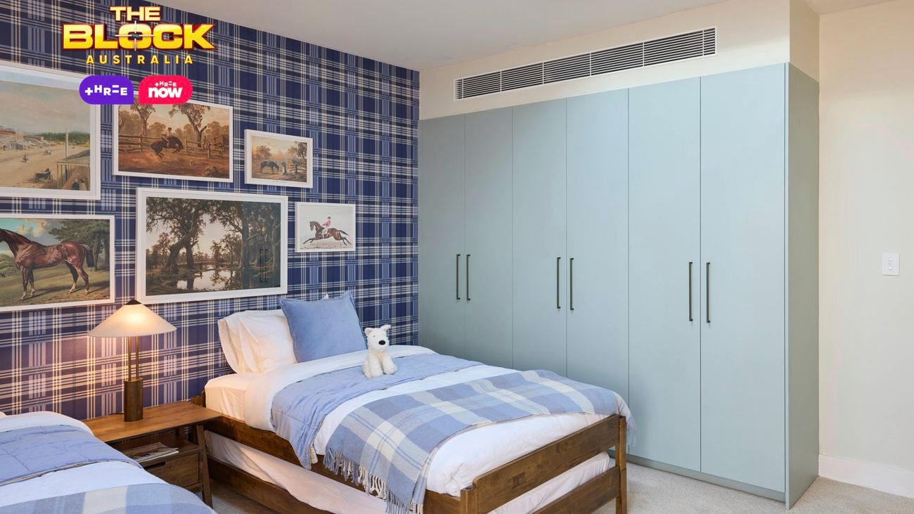 Blue bedroom with a check wallpapered wall and twin beds with blue linens. Above the beds are various horse artworks arranged sporadically and a plae blue wardrobe on the opposite wall.