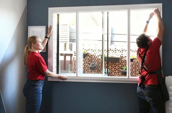 Two people holding a plantation shutter frame against a window
