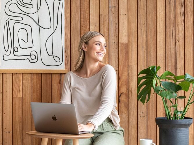 lady on laptop with timber feature wall in back ground and potted plants