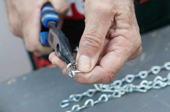 Pliers being used to attach a length of chain to the screw eyes used to hang the vertical garden