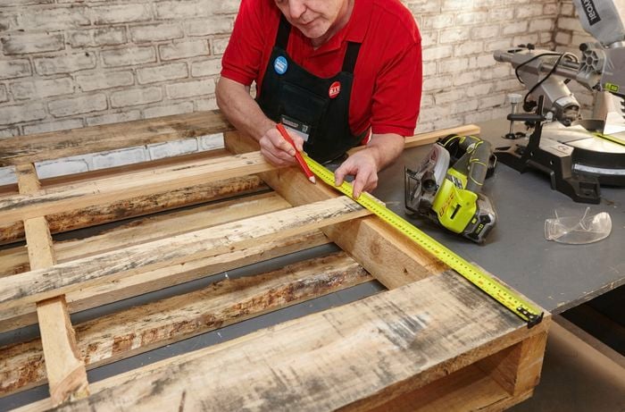 A tape measure being used to mark a wooden pallet for cutting by a Bunnings team member