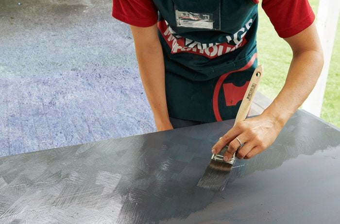 A woman applying a second coat of Rust-Oleum milk paint on a timber desk.