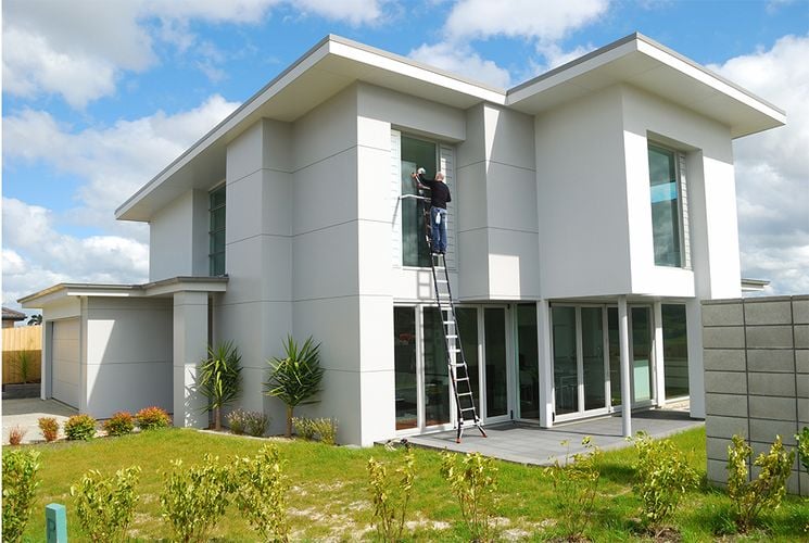 Person cleaning first floor windows while standing on an extendable ladder