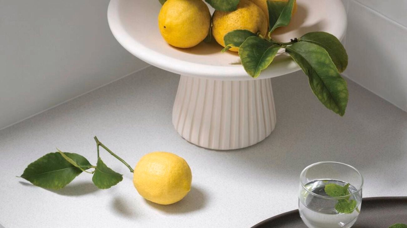 White kitchen bench with gold drawer handles. A platter of lemons, a glass and gray sit on top
