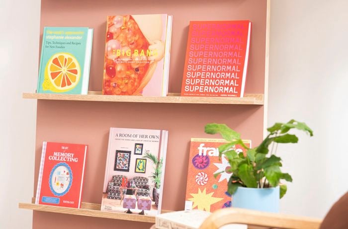 Completed DIY bookshelf with timber ledges displaying books against a painted pink backing panel.
