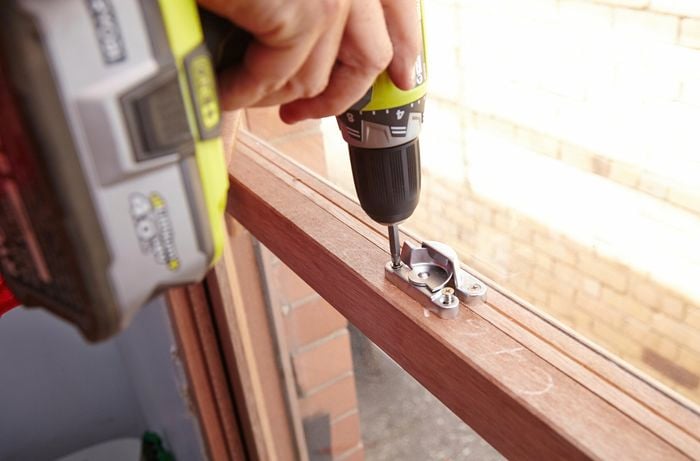 Person using a cordless drill to screw a sash window lock in place