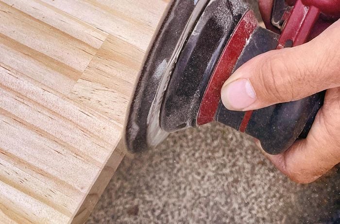 Close up of hands sanding the sides of a pine panel with an orbital sander