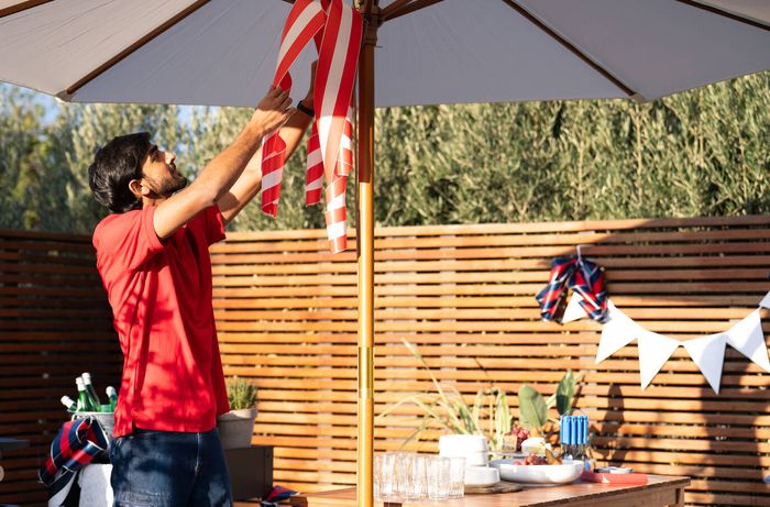 Hanging striped fabric decorations from a patio umbrella in an outdoor entertaining area.