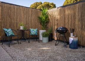 Bamboo screening in an outdoor corner space with an outdoor dining setting, bbq and potted plants.