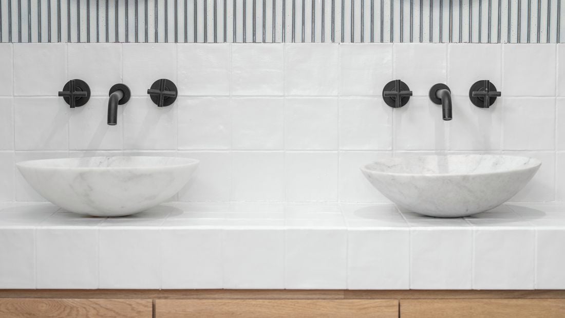 An image of a bathroom with white tiles and black tapware