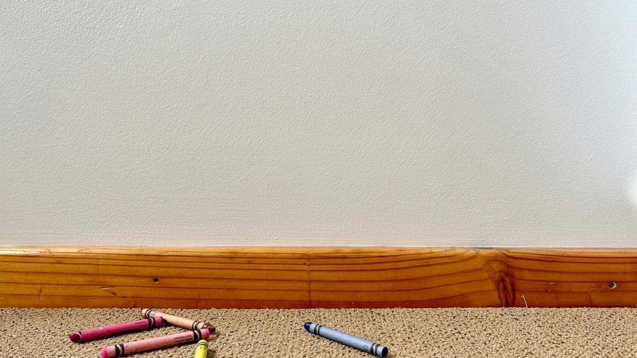 Clean white wall with crayons on the carpet.
