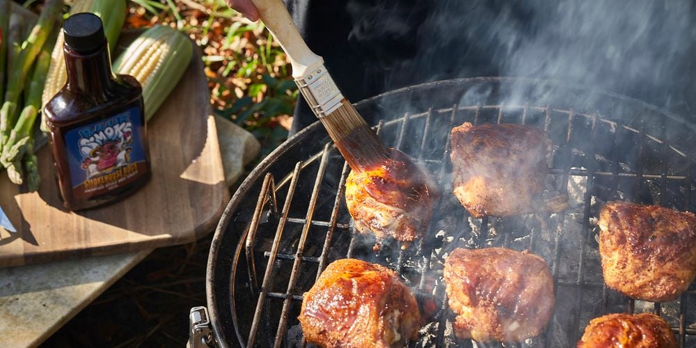 A person marinating some chicken with a brush on a bbq.