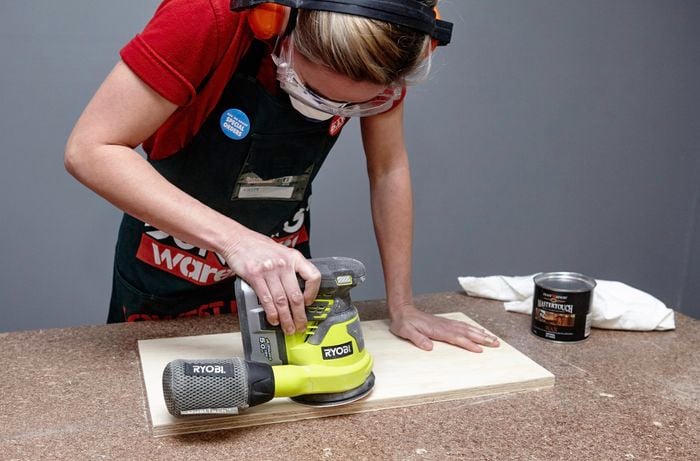 A person sanding a plywood shelf using an orbital sander