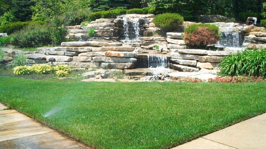 Backyard lawn with sprinklers and waterfall.