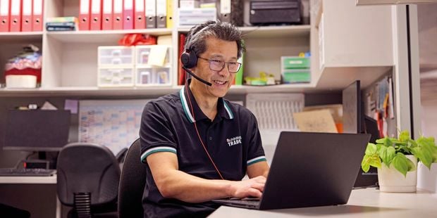 A Bunnings Trade Team Member sitting at a desk with a laptop and a plant on it.