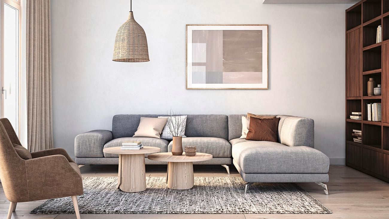 Neutral-coloured living room with a modular couch, rug, bookcase, coffee table, overhead lamp and decorations