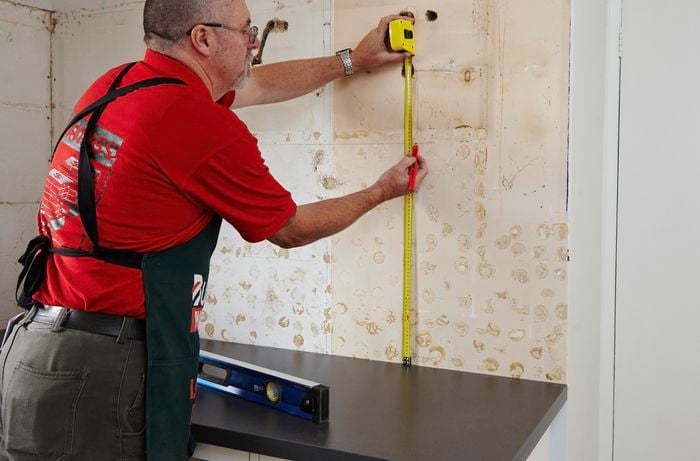 A bare kitchen wall being measured by a Bunnings team member