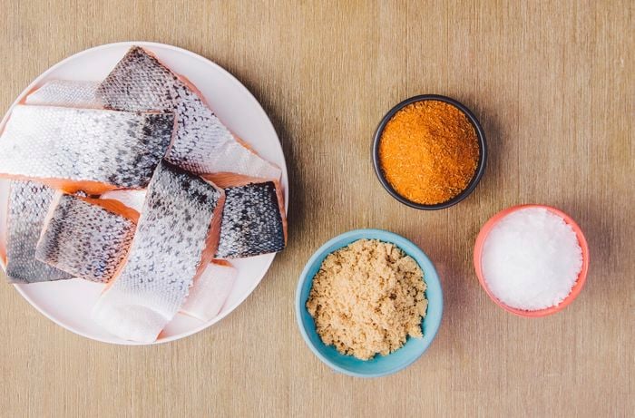 Fillets of salmon on a plate next to bowls of spices