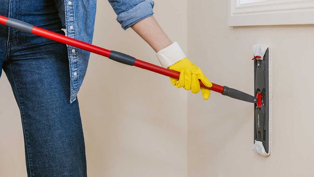 A person cleaning a wall with a flat mop.