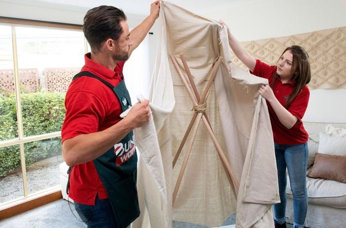 Two people draping tepee structure with cloth material to form play tent.