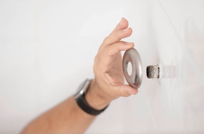 A person holds the removed shower plate cover on the wall.