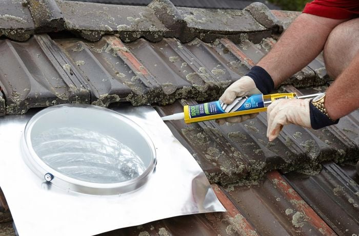 Silicone gap filler being used to waterproof the skylight flashing's edge with the roof tiles below