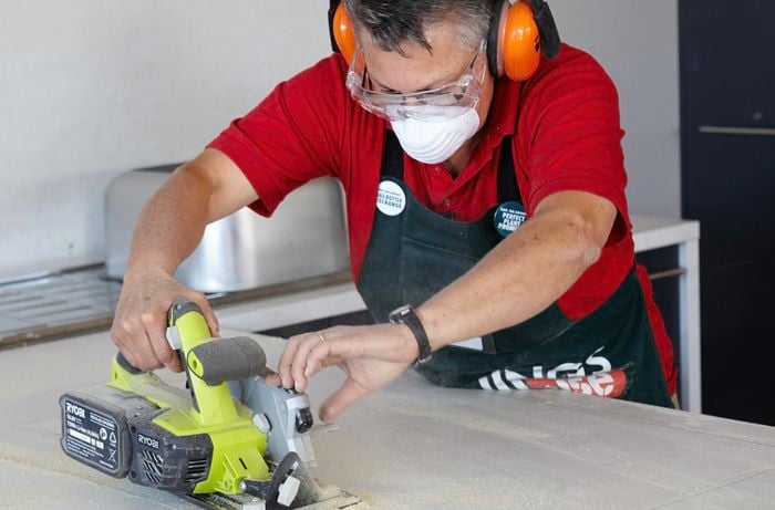 Person cutting kitchen benchtop with handsaw.