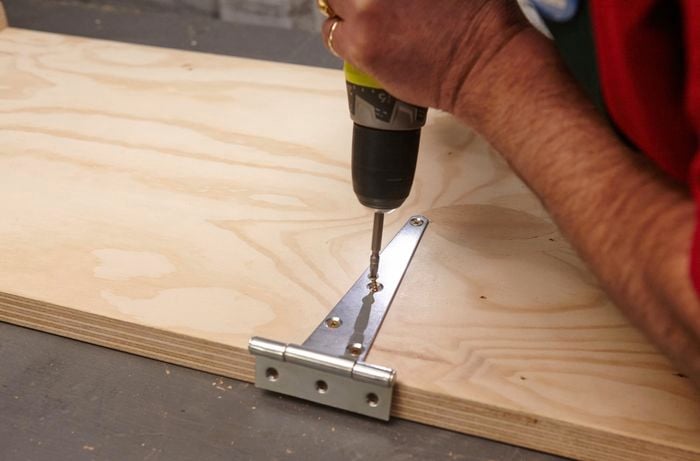 Person attaching hinge to timber with drill.