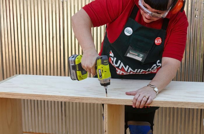 The inner shelves of a laundry basket dresser being secured in place with a drill