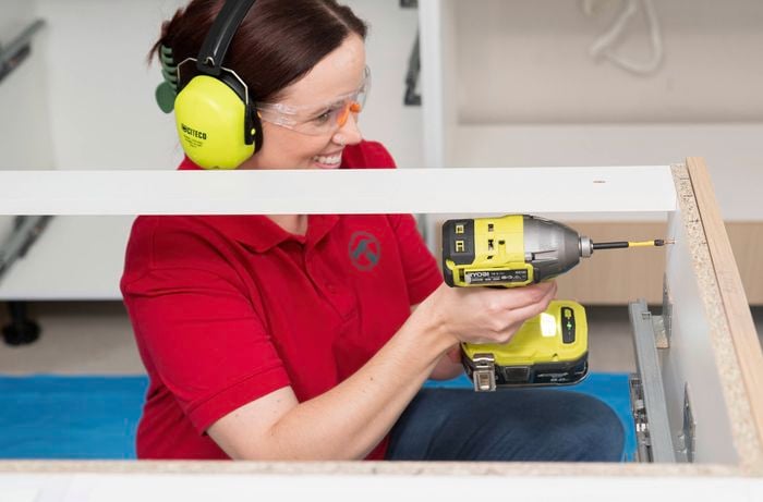 A Bunnings Team Member wearing safety gear is assembling a flat-pack cabinet using a power drill during a kitchen renovation.