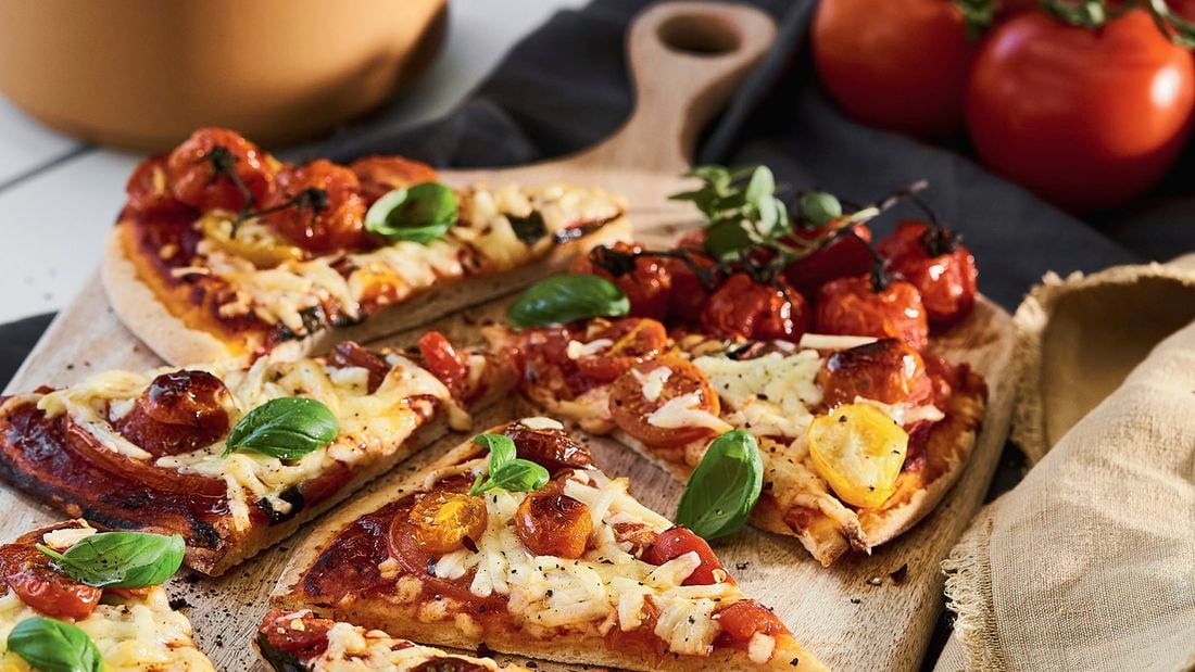 A cooked vegan margherita pizza cut into slices displayed on a wooden serving board with handle