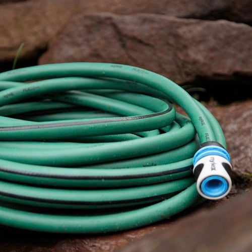 Green Nylex garden hose with a tap fitting fitted on endsits coiled on some garden paving rocks