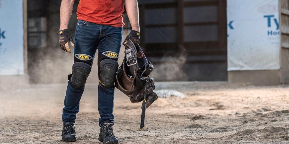 A person on site wearing gloves, kneepads and holding a toolbelt