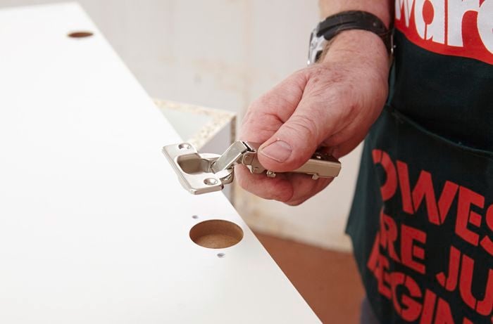 Person holding hinge against kitchen cabinet door.
