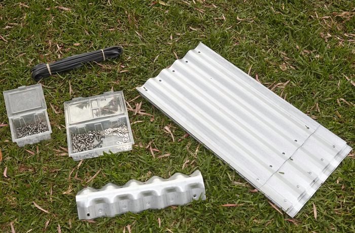 Corrugated iron, nuts and bolts, and protective edging, lying on the grass.