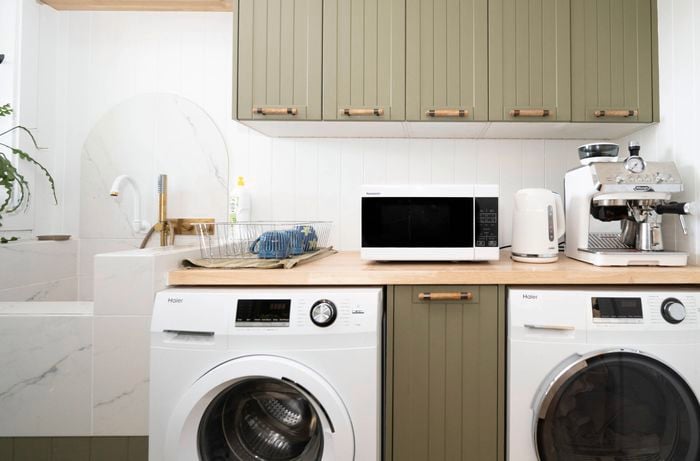 The image shows a laundry used as a temporary kitchen, equipped with essentials like a kettle, microwave, and toaster while the main kitchen is being renovated.