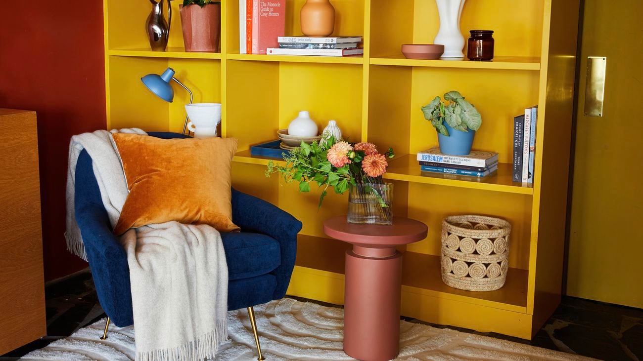 Vibrant reading corner including a bright yellow bookcase and a rich navy velvet armchair
