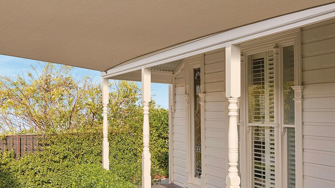 An outdoor area is covered but a beige, shade sail connected to the side of a house