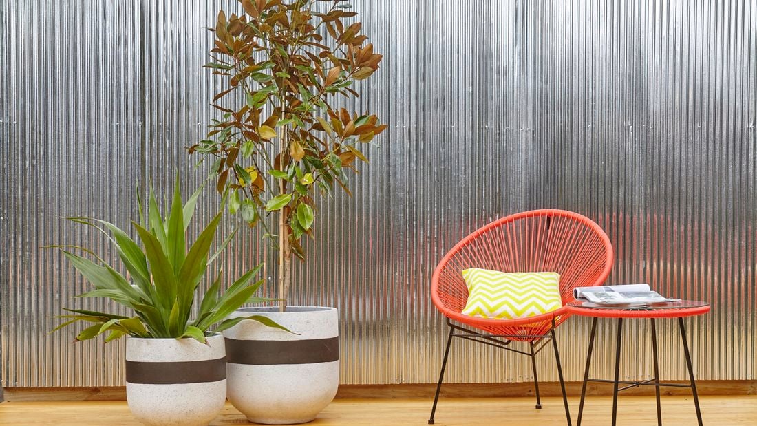 Outdoor furniture and potted plants in front of a wall of vertical corrugated iron