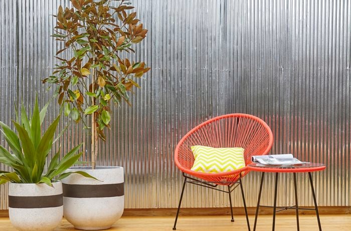 Outdoor furniture and potted plants in front of a wall of vertical corrugated iron