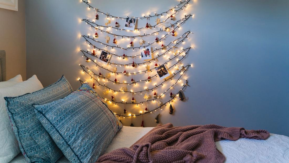 Fairy lights zig zagging down a bedroom wall with polaroid pictures and christmas decorations attached throughout it