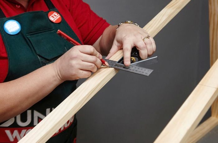 Person using metal ruler and pencil to make a mark on a length of timber.