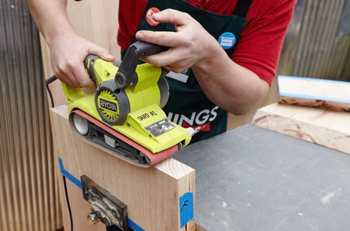 A person sanding the end of a piece of hardwood with a belt sander
