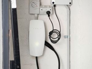 A Tesla Wall Connector is mounted on a wall, neatly installed with connected power cables. 