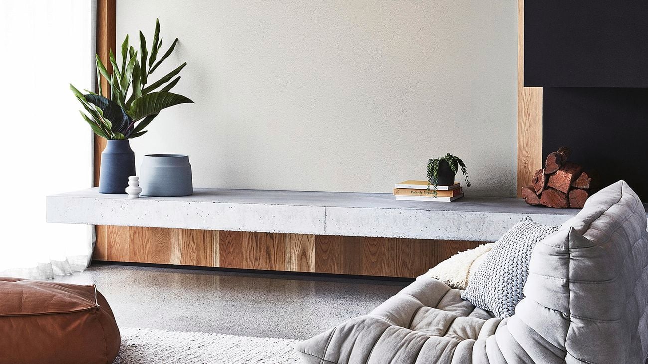 Modern living room area with stone entertainment unit with plants and other decor on top.
