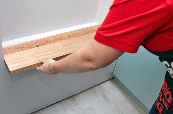 Person inserting wooden shelf at the bottom of wall niche.