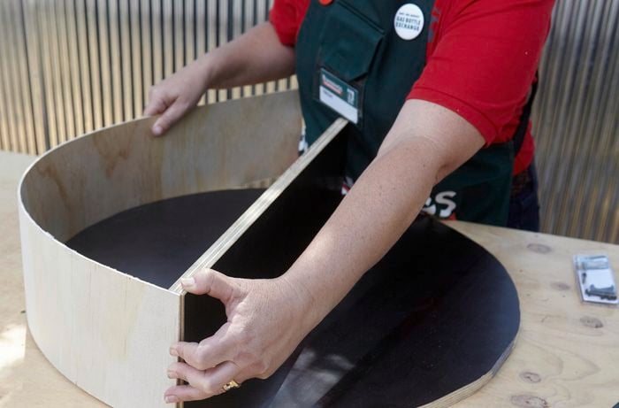 A person curving a strip of plywood around a circular plywood base with a shelf