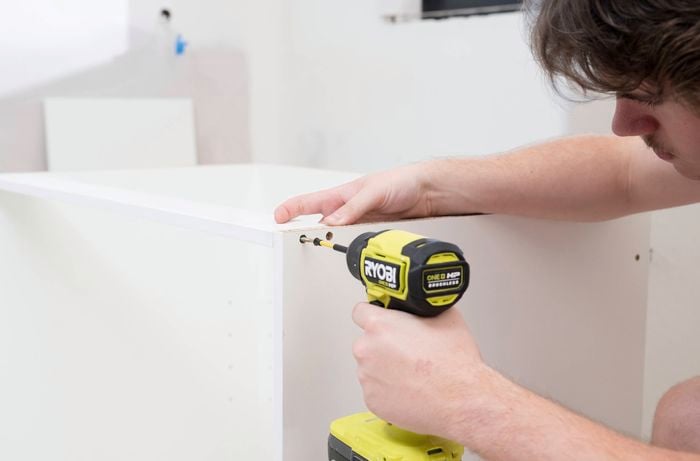  A person uses a power drill to secure an internal support rail to a corner base cabinet.